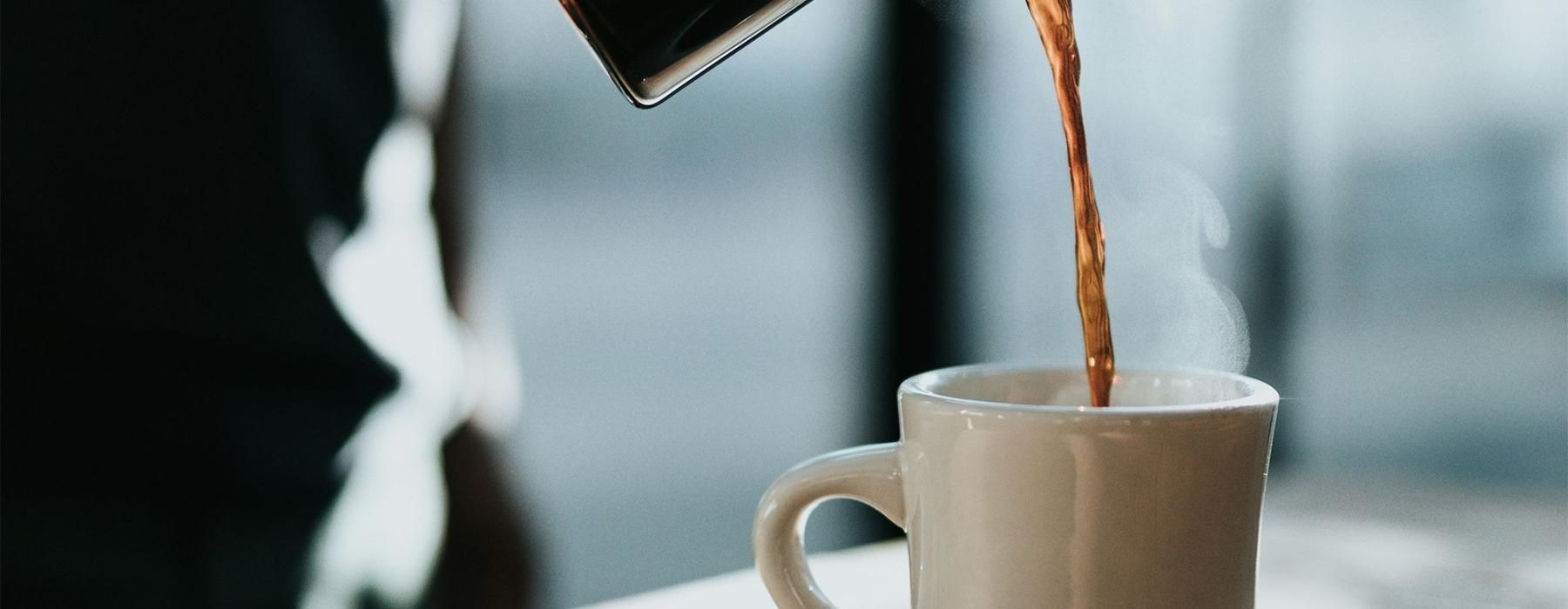 a person pouring a carafe of coffee into a cup